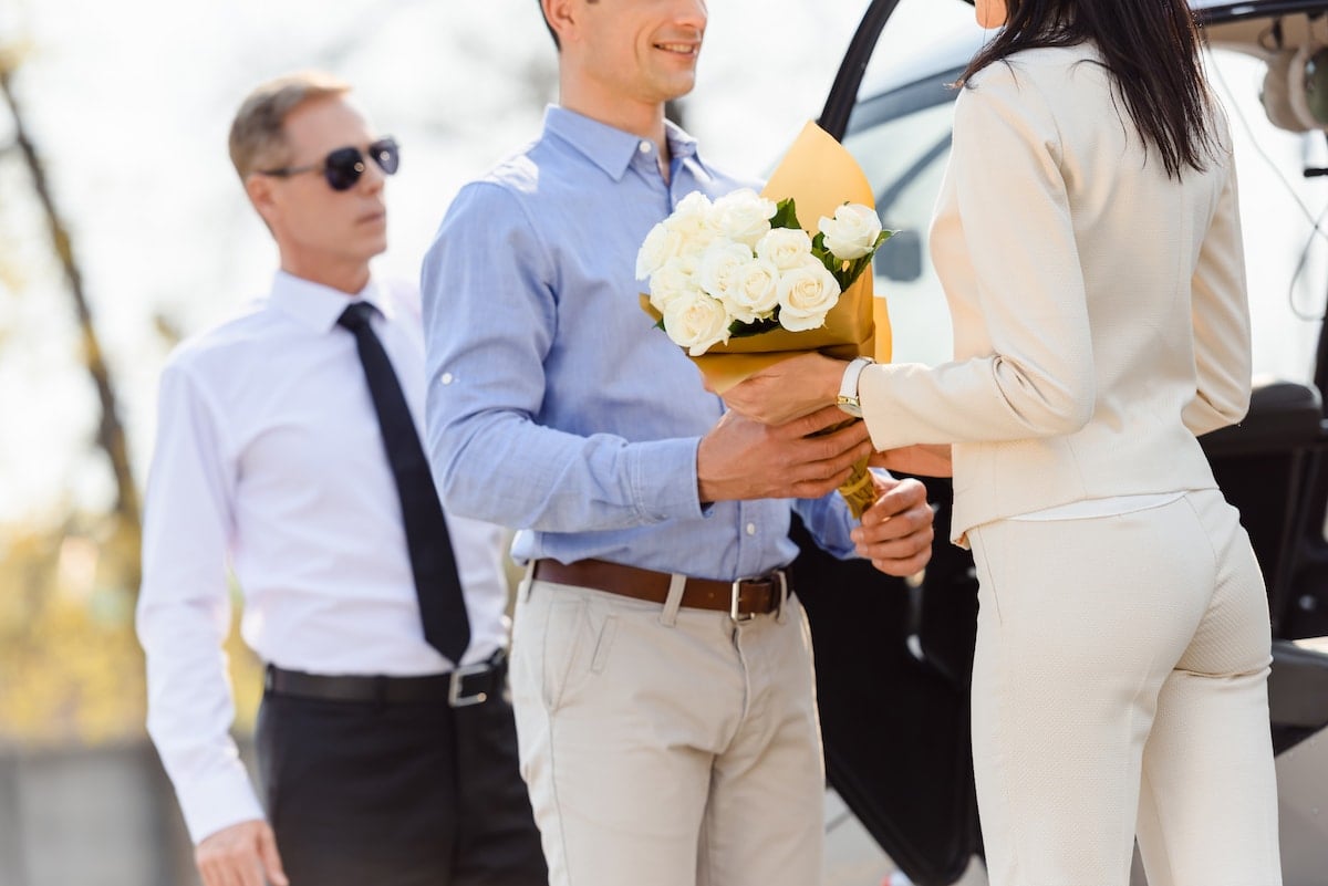 A young man giving flowers to a woman in front of a helicopter. 