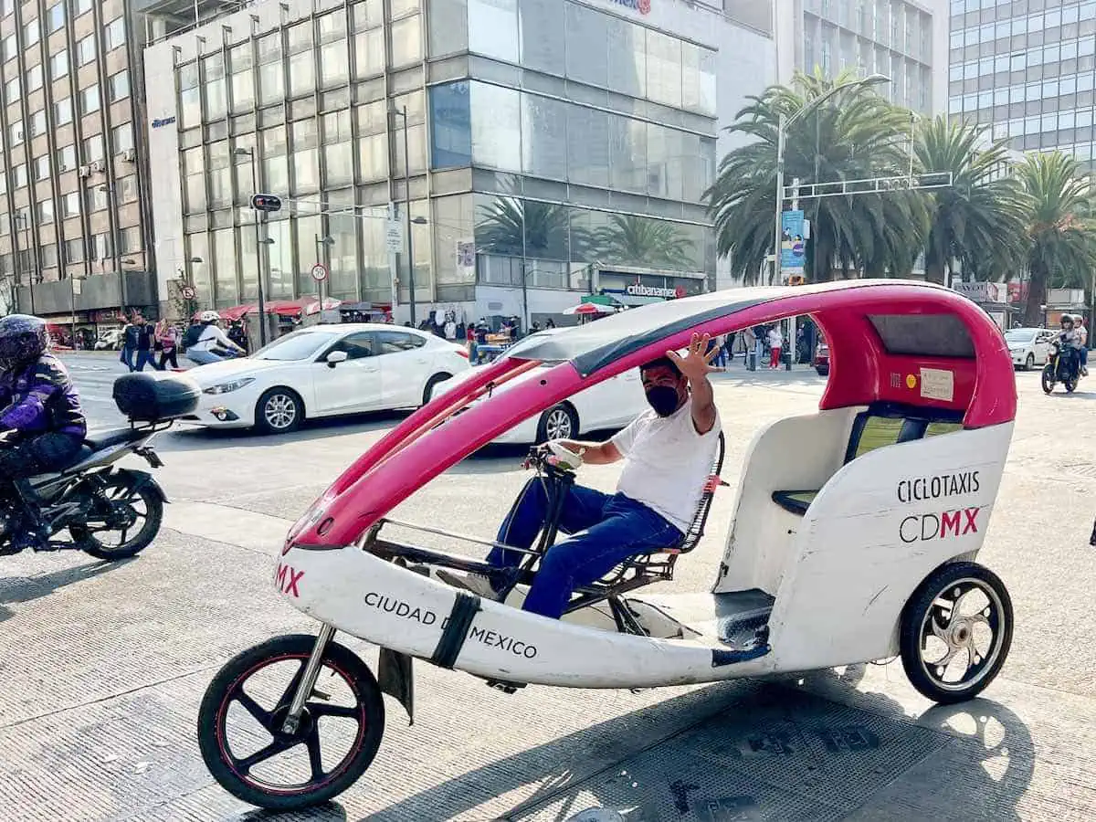 A ciclotaxi driver waving from inside his tuk-tuk in Mexico City. 