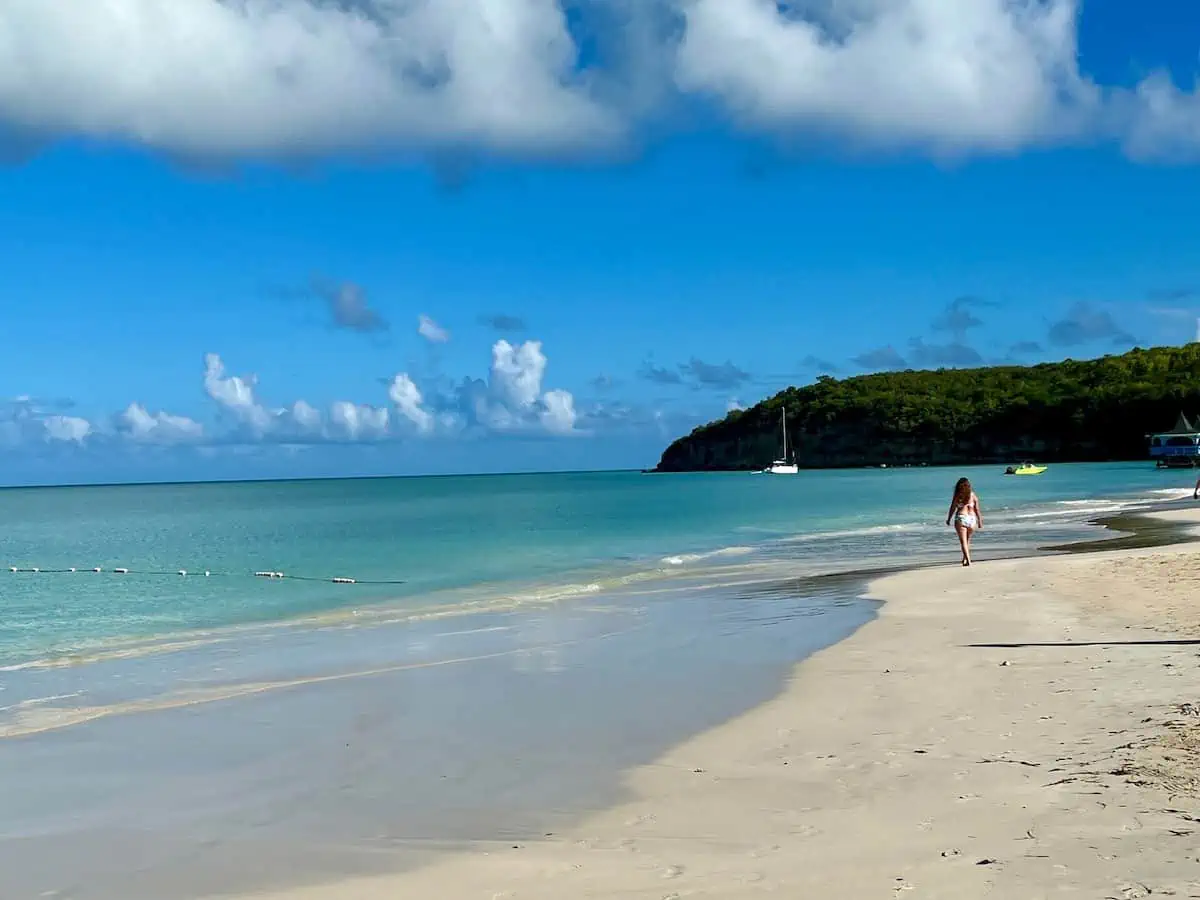 A lady walking along shore with sailboat in the distance.