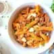 A bowl of pasta with sundried tomatoes and eggplant on the table with parsley garnish.