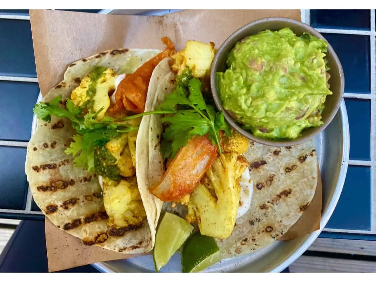 Two tacos with grill marks on a white plate with a side of guacamole.