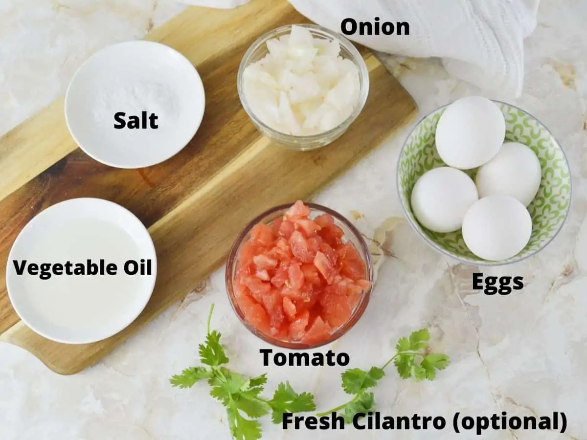 Ingredeints for scrambled eggs with tomato and onion including vegetable oil and salt.