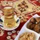 A glass of Turkish tea with nuts on a white plate on a red rug.